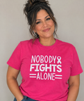 Woman wearing a pink tee with white Nobody Fights Alone lettering and an awareness ribbon.