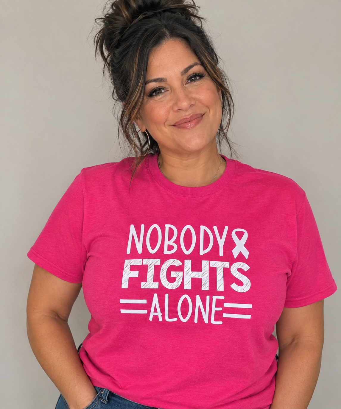 Woman wearing a pink tee with white Nobody Fights Alone lettering and an awareness ribbon.